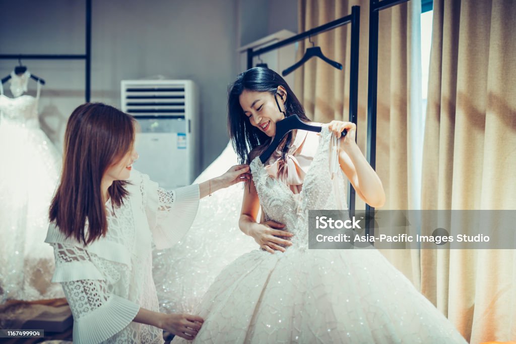 Two Asian Young women shopping for wedding dress gowns in boutique discount store, many white garments hanging on rack hangers row. Wedding Dress, Dress, Shopping, Store, Women, Asian and Indian Ethnicities, Shanghai Wedding Stock Photo