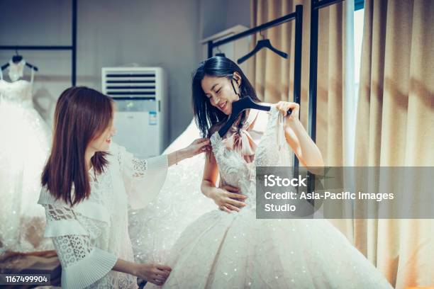 Two Asian Young Women Shopping For Wedding Dress Gowns In Boutique Discount Store Many White Garments Hanging On Rack Hangers Row Stock Photo - Download Image Now