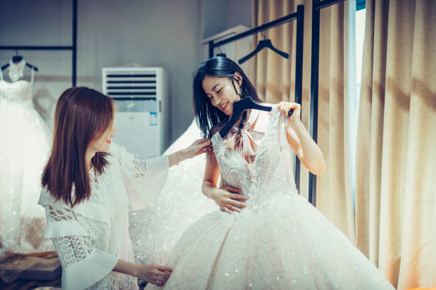 dwie azjatyckie młode kobiety zakupy suknie ślubne w butikowym sklepie dyskontowym, wiele białych ubrań wiszących na wieszakach rack wiersz. - suknia ślubna zdjęcia i obrazy z banku zdjęć