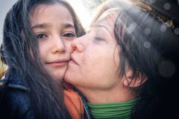 Close up mother and daughter portrait of little girl and young woman over sunny background