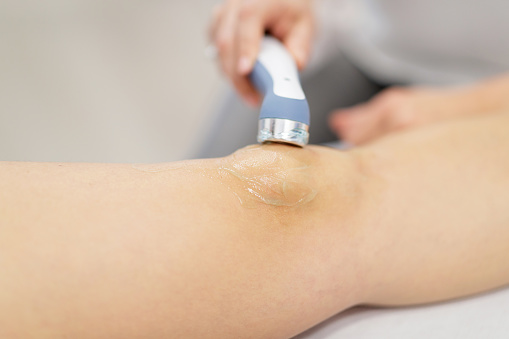 Human knee with applied gel undergoing gentle ultrasound treatment