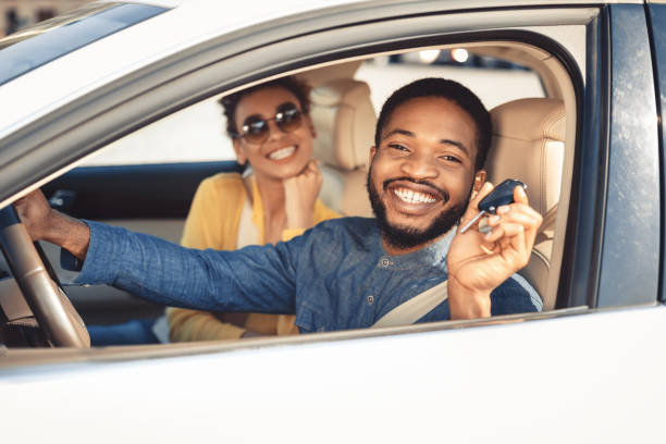 zwiedzanie salonu samochodowego. afro para pokazująca klucz do samochodu - car car rental car dealership key zdjęcia i obrazy z banku zdjęć