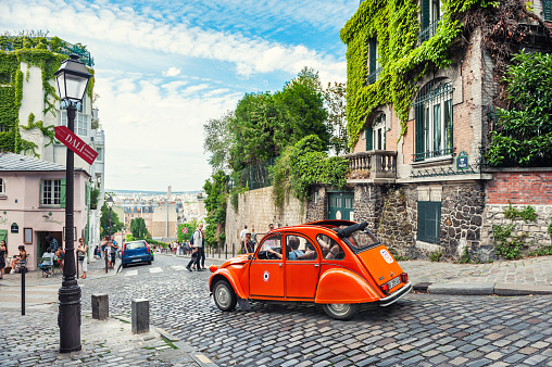 Paris, France - July, 21, 2019: Beautiful old street in Montmartre district in Paris, France. Orange retro car goes down the street.