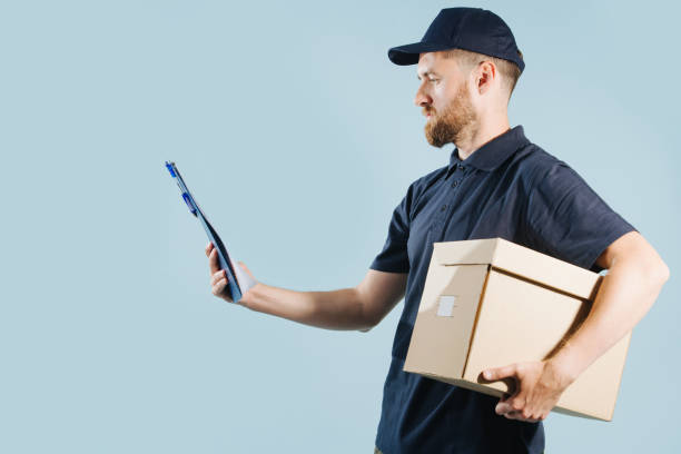 istock Delivery man in uniform is checking his orders list while holding box under arm 1167505701