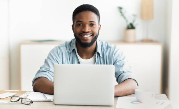 istock African guy using laptop, smiling and drinking coffee in office 1167506514