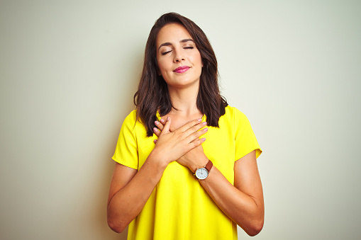 Young beautiful woman wearing yellow t-shirt standing over white isolated background smiling with hands on chest with closed eyes and grateful gesture on face. Health concept.