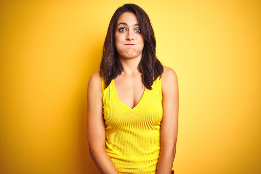 Young beautiful woman wearing t-shirt standing over yellow isolated background puffing cheeks with funny face. Mouth inflated with air, crazy expression.
