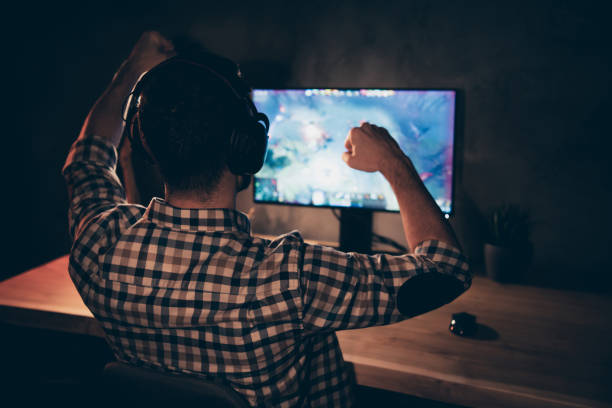 istock Close up back rear behind view photo he him his guy videogame talk headset microphone strategy raise fist hand arm hopeful speech team wear casual plaid checkered shirt internet cafe table indoors 1167509397