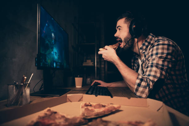 istock Close up side profile view photo he him his guy videogame headset microphone teammates concentrated look screen hand arm put pizza slice mouth wear casual plaid checkered shirt cafe table indoors 1167509584