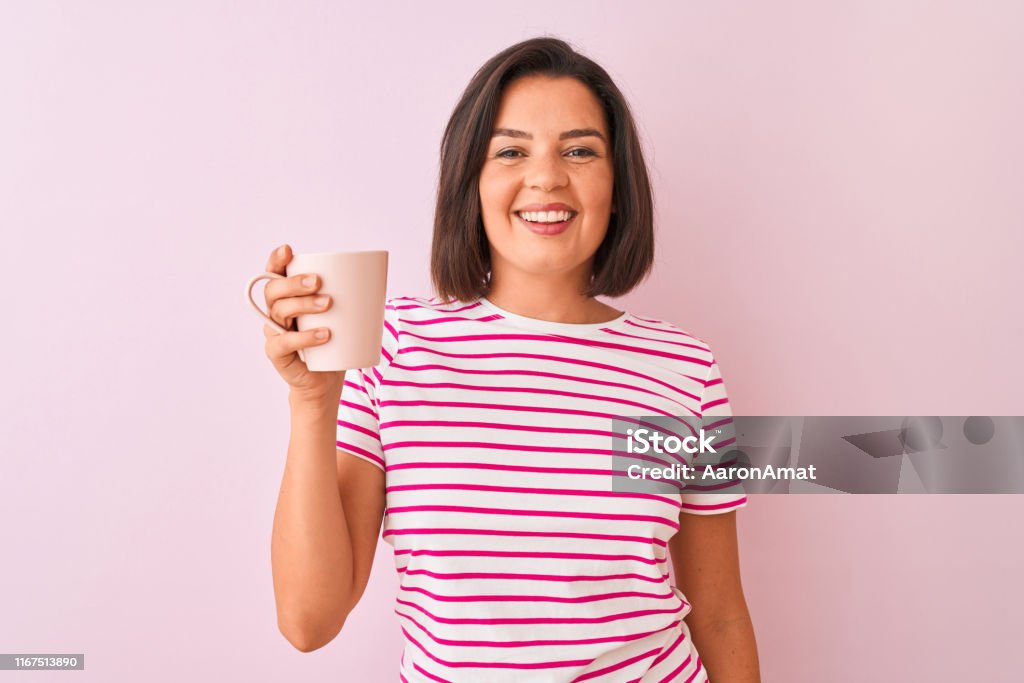 Copo bebendo da mulher bonita nova do café que está sobre o fundo cor-de-rosa isolado com uma face feliz que está e que sorri com um sorriso confiável que mostra os dentes - Foto de stock de Caneca royalty-free Copo bebendo da mulher bonita nova do café que está sobre o fundo cor-de-rosa isolado com uma face feliz que está e que sorri com um sorriso confiável que mostra os dentes - Foto de stock de Caneca royalty-free