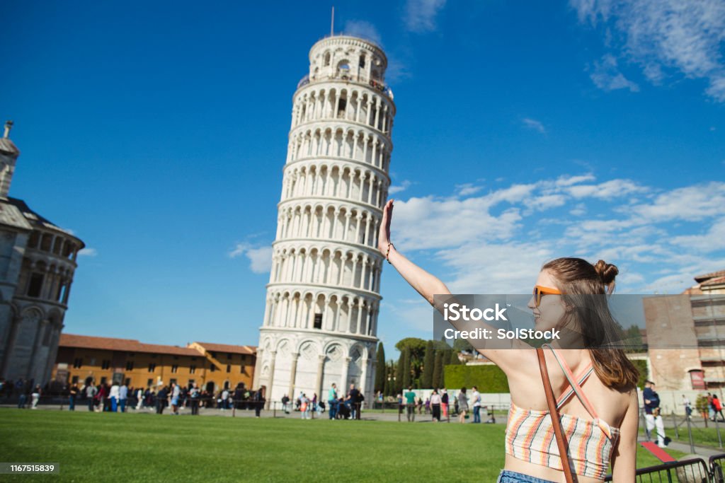 Discovering Historic Italy A woman is gesturing with her hands in front of the Leaning Tower of Pisa. Leaning Tower of Pisa Stock Photo