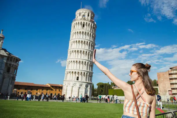 A woman is gesturing with her hands in front of the Leaning Tower of Pisa.
