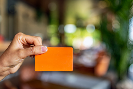 Close up of a female hand holding blank orange note card sign. Closeup of  female hand holding plastic credit card, woman showing blank business card, copy space.