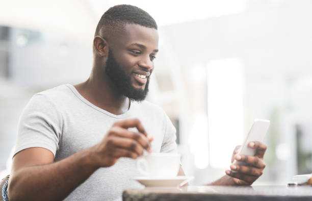 istock Bearded african man with cup of coffee reading on cellphone 1167517758