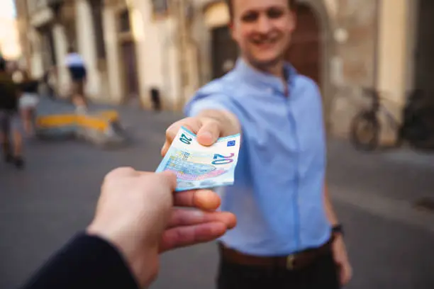 The focus is on the foreground, of the man's hand as he passes over cash in the street.