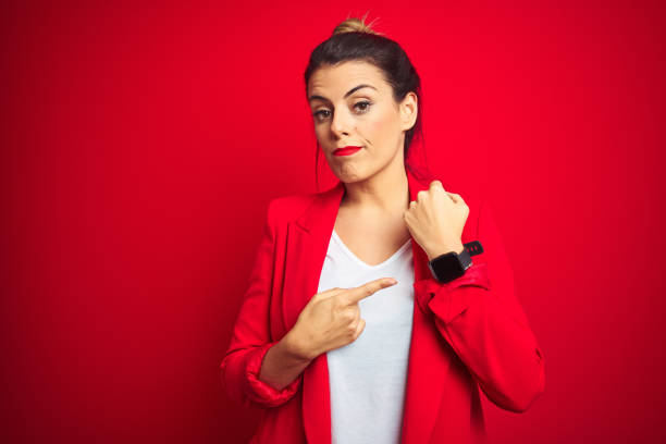 young beautiful business woman standing over red isolated background in hurry pointing to watch time, impatience, looking at the camera with relaxed expression - clock face clock deadline human hand imagens e fotografias de stock