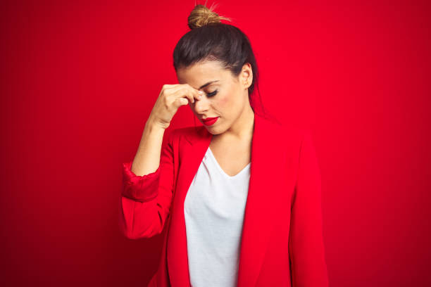 young beautiful business woman standing over red isolated background tired rubbing nose and eyes feeling fatigue and headache. stress and frustration concept. - dull colors imagens e fotografias de stock