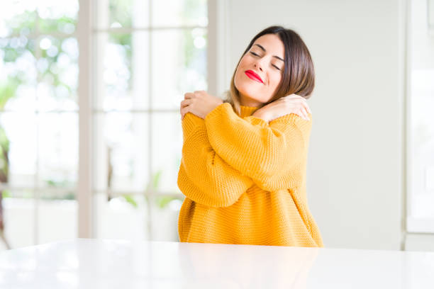young beautiful woman wearing winter sweater at home hugging oneself happy and positive, smiling confident. self love and self care - self love imagens e fotografias de stock