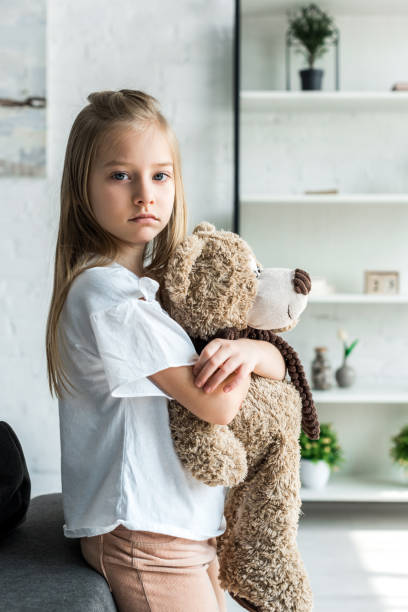 istock cute kid looking at camera and holding teddy bear at home 1167527023