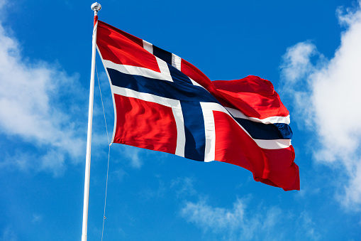 national flag of Norway blowing in the wind in front of a blue sky