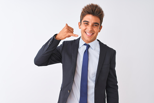 Young handsome businessman wearing suit standing over isolated white background smiling doing phone gesture with hand and fingers like talking on the telephone. Communicating concepts.