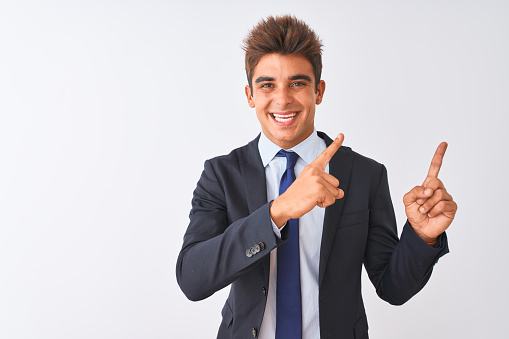 Young handsome businessman wearing suit standing over isolated white background smiling and looking at the camera pointing with two hands and fingers to the side.