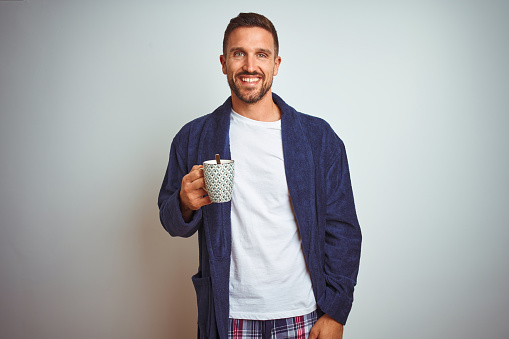 Man wearing comfortable pajamas and robe drinking cup of coffee over isolated background screaming proud and celebrating victory and success very excited, cheering emotion