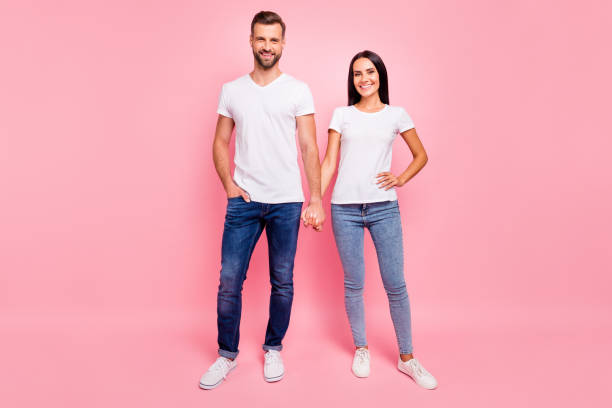 full length body size photo of glad funky couple standing hand in hand while isolated with pastel background - shirt women pink jeans imagens e fotografias de stock