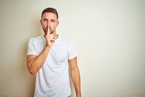 Young handsome man wearing casual white t-shirt over isolated background asking to be quiet with finger on lips. Silence and secret concept.