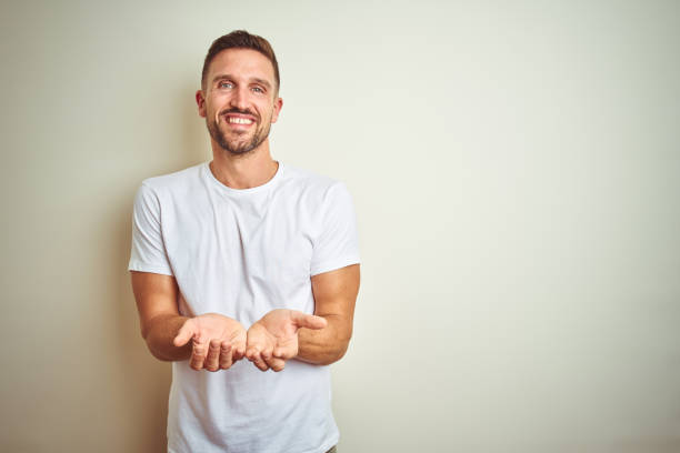 Young handsome man wearing casual white t-shirt over isolated background Smiling with hands palms together receiving or giving gesture. Hold and protection Young handsome man wearing casual white t-shirt over isolated background Smiling with hands palms together receiving or giving gesture. Hold and protection hand palm stock pictures, royalty-free photos & images