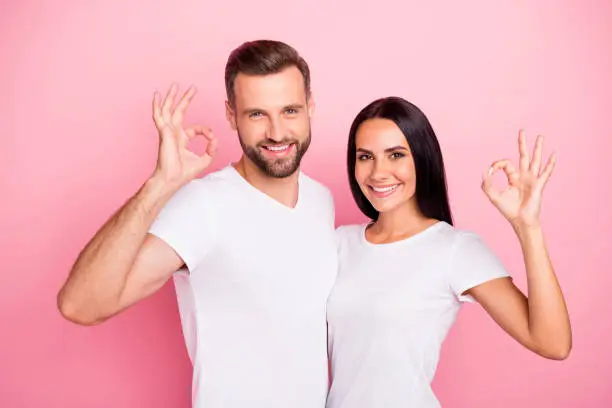 Portrait of his he her she two nice attractive lovely charming cute cheerful cheery spouses embracing, showing ok-sign cool ad advert isolated over pink pastel background
