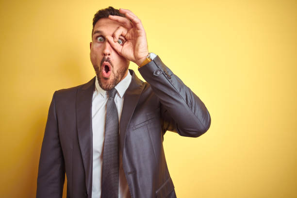 istock Young handsome business man over yellow isolated background doing ok gesture shocked with surprised face, eye looking through fingers. Unbelieving expression. 1167536308