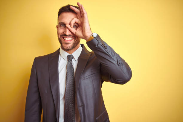 istock Young handsome business man over yellow isolated background doing ok gesture with hand smiling, eye looking through fingers with happy face. 1167536311
