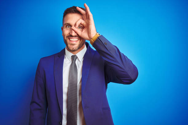 istock Young handsome business man over blue isolated background doing ok gesture with hand smiling, eye looking through fingers with happy face. 1167536405