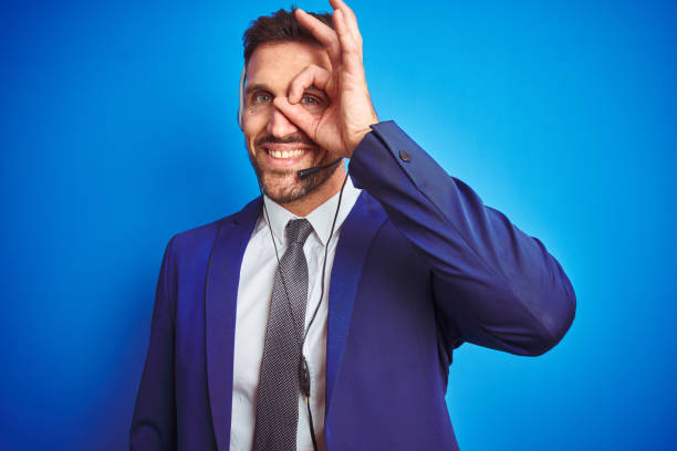 istock Young handsome operator man wearing call center headset over blue isolated background doing ok gesture with hand smiling, eye looking through fingers with happy face. 1167536604