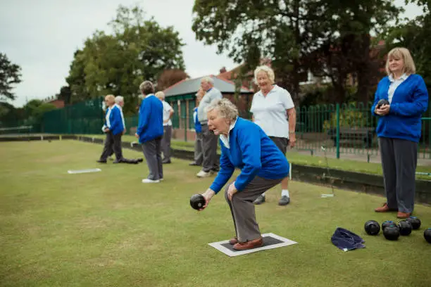 A side view shot of a senior woman playing lawn bowling with other seniors.