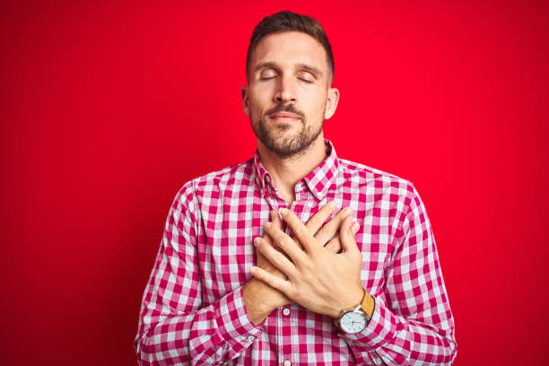 istock Young handsome man over red isolated background smiling with hands on chest with closed eyes and grateful gesture on face. Health concept. 1167539686