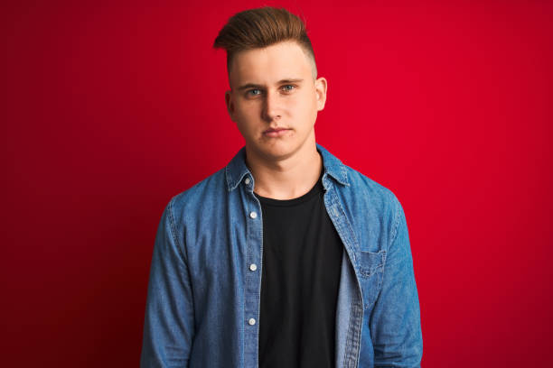 istock Young handsome man wearing denim shirt standing over isolated red background Relaxed with serious expression on face. Simple and natural looking at the camera. 1167545868