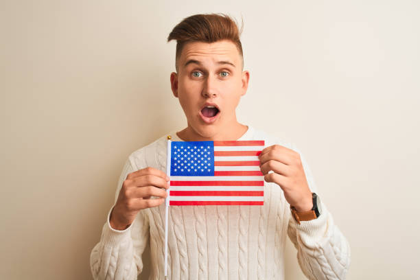 istock Young handsome man holding USA flag over isolated white background scared in shock with a surprise face, afraid and excited with fear expression 1167546857