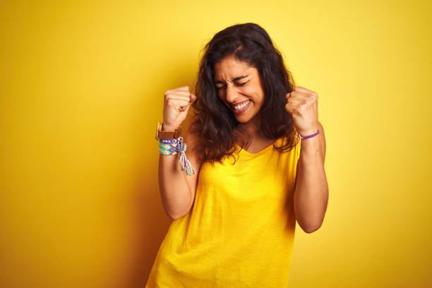 t-shirt desgastando da mulher bonita nova que está sobre o fundo amarelo isolado muito feliz e excitado que faz o gesto do vencedor com os braços levantados, sorrindo e gritando para o sucesso. conceito da celebração. - cheerful happiness facial expression behavior - fotografias e filmes do acervo