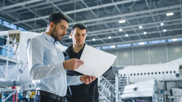 istock Aircraft Maintenance Worker and Engineer having Conversation. Holding Project Blueprint. 1167549612