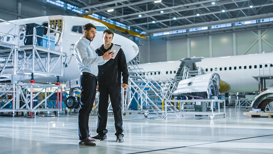 Aircraft Maintenance Worker and Engineer having Conversation. Holding Tablet.