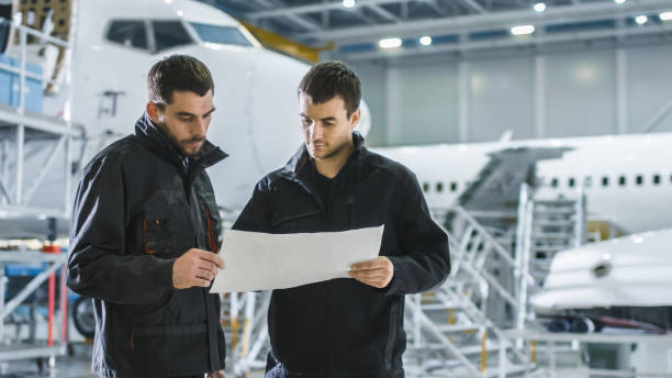 istock Aircraft Maintenance Worker and Engineer having Conversation. Holding Project Blueprint. 1167549679