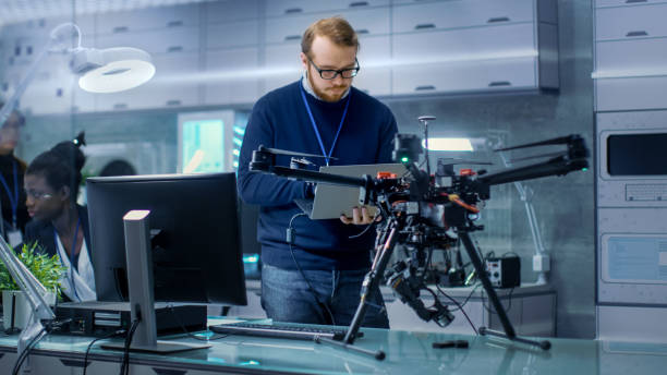 istock Young Male Engineer Programs Drone while Holding Laptop in His Hands. He Works in a Bright Modern High-Tech Laboratory. 1167549760