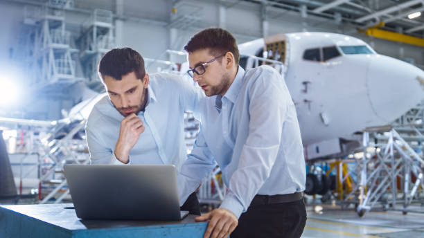 Two Aircraft Mechanics Working and Having Conversation next to Laptop Computer Two Aircraft Mechanics Working and Having Conversation next to Laptop Computer air vehicle stock pictures, royalty-free photos & images