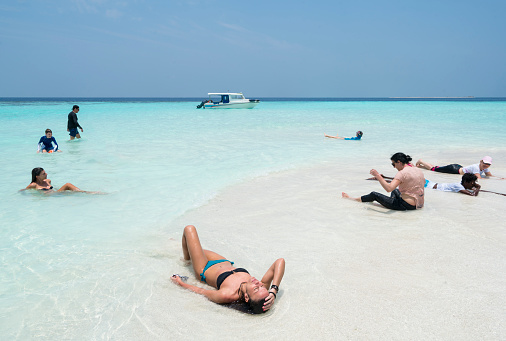 Tourist, young and senior woman, enjoying laying, sitting in water of  Sand bank, small sand island surrounded with beautiful  turquoise water  in April, Maldives. The island is located not far from Maafushi island, Maldives. It is tropical paradise island, one of places for visiting from Maafushi Island on day tour by boat.