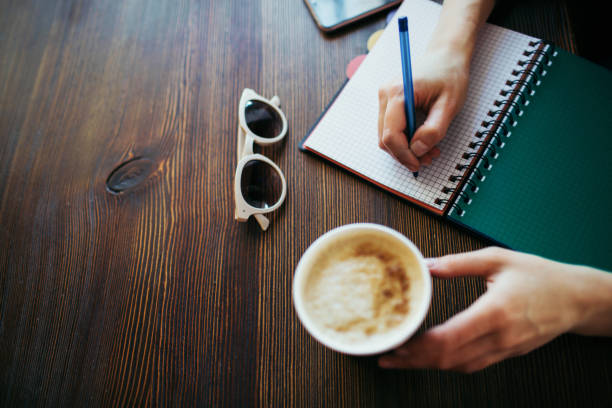 istock Overview of woman's hands writing in a notepad, holding coffee. 1167550393