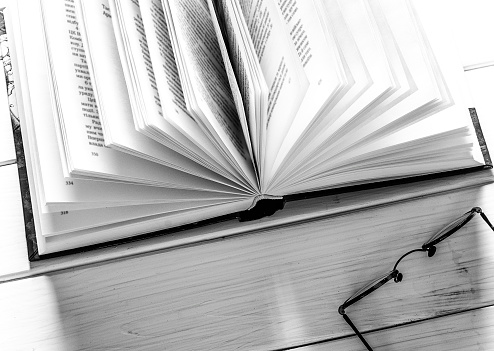 Open book ready to read lies on a white wood table next to the old round glasses. closeup