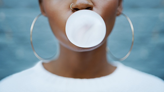 Shot of an unrecognizable woman blowing a bubble with her gum against a grey background outdoors