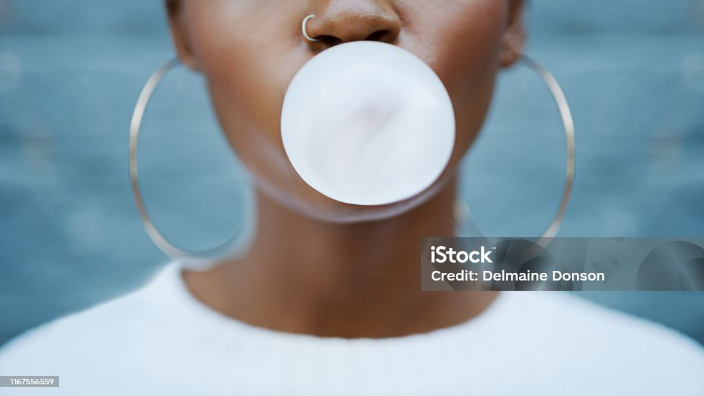 Talk is cheap Shot of an unrecognizable woman blowing a bubble with her gum against a grey background outdoors Bubble Gum Stock Photo